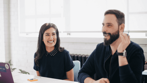 Two smiling people sit at a conference table