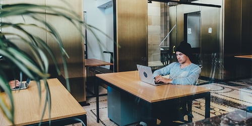 Person sits at a table on their laptop in an empty office.