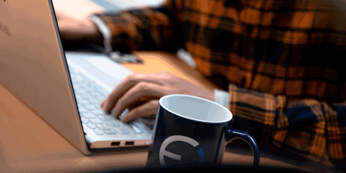 A person sits working at a computer with only their hands in view while drinking coffee. 