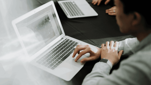 A person sits down with their arms crossed typing on their laptop.