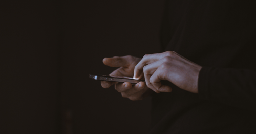 Someone with only their hands in view is scrolling on their phone with a brightly lit screen.