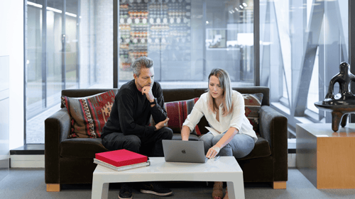 Two people sitting on a couch focused on a laptop sitting on a small table.