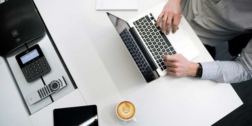 Someone works on their laptop accompanied by their coffee and a notepad