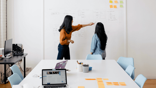 Two people stand at a board categorizing different notes they've made