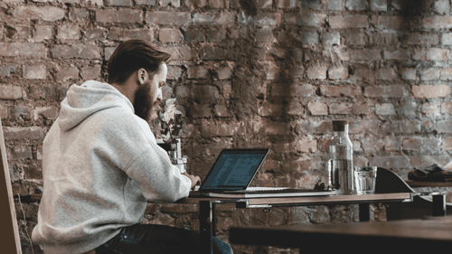 A person sits at a tables working on their laptop in a cafe. 