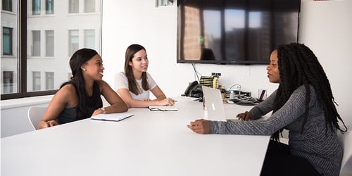 A group of people sit in a conference room having a discussion across from one another. 