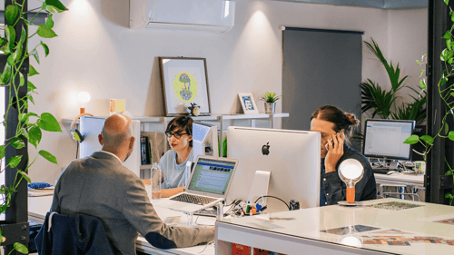 Three people sit working at their desks in a work pod.