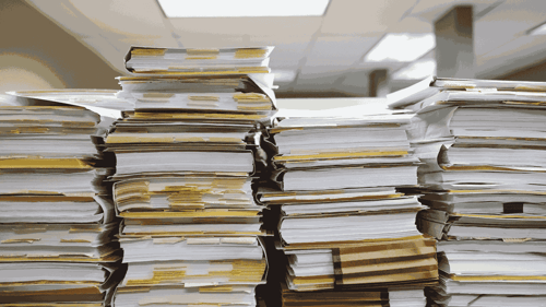 A stack of books with notes and pages hanging out of them sit on top of a table in an office. 