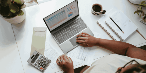 A person with their hands in view sits at their computer working on a spreadsheet. 