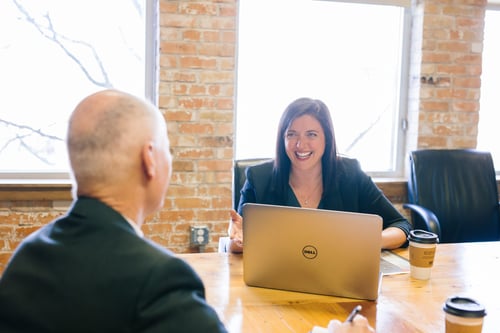 Two people sit across from one another at a conference tables laughing and taking notes