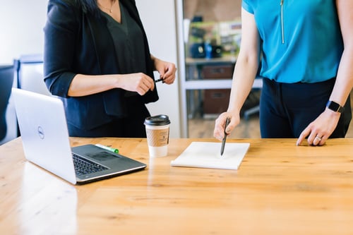 Two people stand next to a table discussing the paperwork in front of them