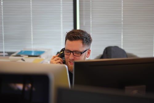 A person works at their desk while taking a phone call