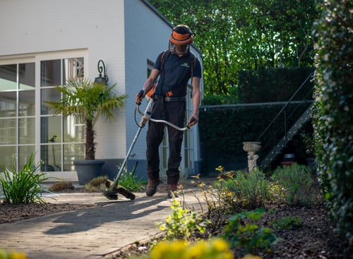 A landscaper uses their weedwacker along the edgeway outside of a home