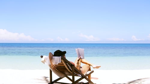 A person sits on a beach reclined in a beachair while reading a book