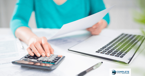 A person sits reviewing information with paperwork in one hand and using a calculator with the other