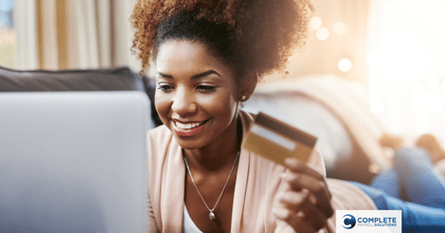 A person is smiling and looking at their computer screen with their debit card in hand