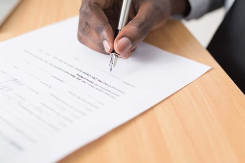 A person rests their hand on a table while signing paperwork