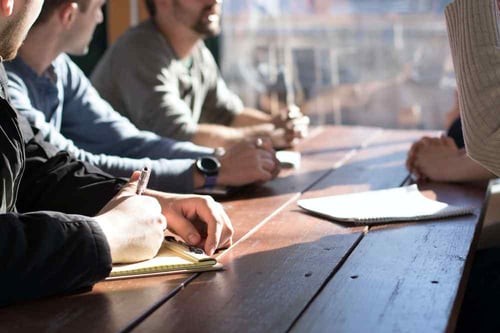 Group of people sitting at a table discussing and taking notes 