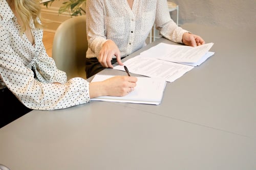 Two people sit at a desk together reviewing paperwork