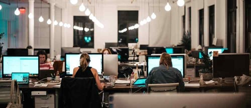 A group of people word at their computers in a large industrial office building