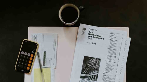 A pile of tax forms on a desk accompanied by a cell phone and a cup of coffee