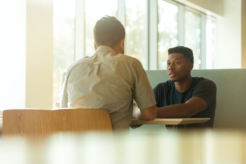 Two people have a discussion at a small table across from one another