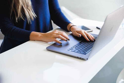 A person sits at their desk typing on their laptop