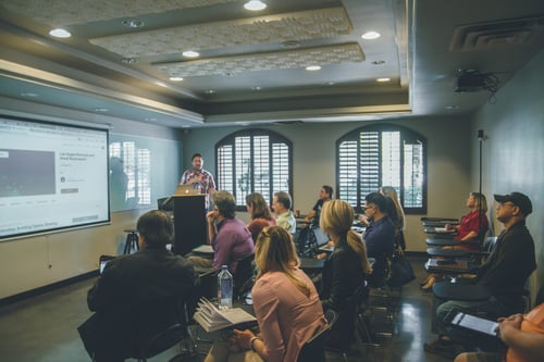 A group of people pay attention to a presenter in a classroom setting