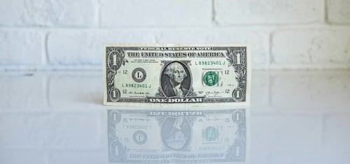 A dollar bill is suspended upright against a brick wall