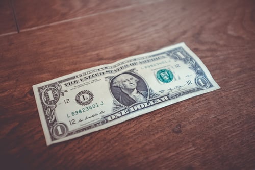 A dollar bill is placed flat on a wood table