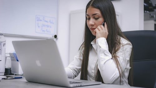 A person talks on their cell phone while working at their computer