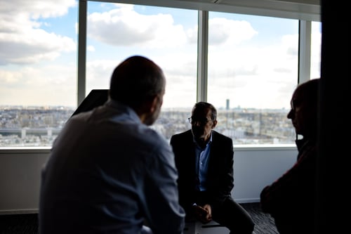 A group of people sit in a dimly lit conference room having a conversation.