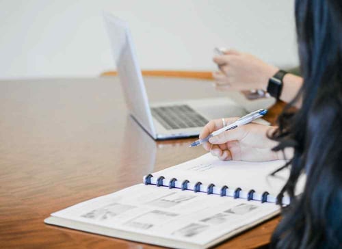 Two people work together. One works on a computer while the other takes notes on their laptop.