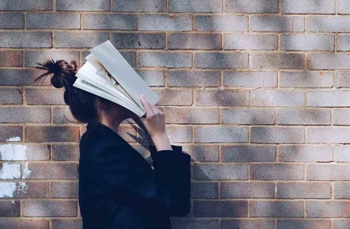 A person stands in front of a brick wall with papers covering their face.