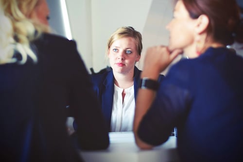 Two people sit with their backs facing the shot while having a conversation across a table from another person