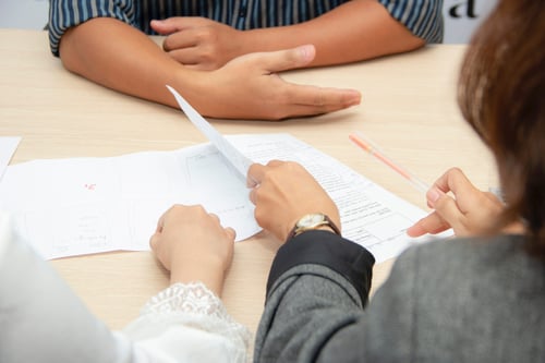 Two people reviewing paperwork sit across the table from another individual having a discussion