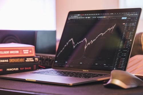 A laptop sits on a desk with stock market information pulled up on the screen