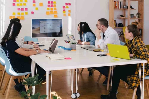 A group of people sit in a conference room reviewing information on a television screen that is surrounded by colorful adhesive notes