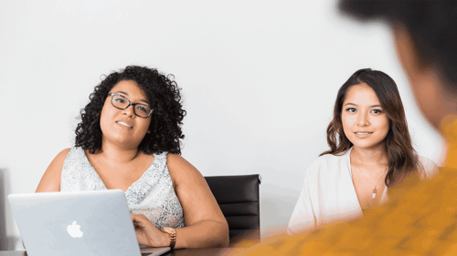 Two people sit across the table from another person not in view conducting a job interview.