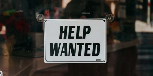 An employer posted a help wanted sign in their front window shop.