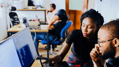 Two people sit together looking at a computer working collaboratively.