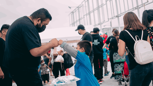 Two people are in focus giving one another a fist bump, while others are walking past around them.