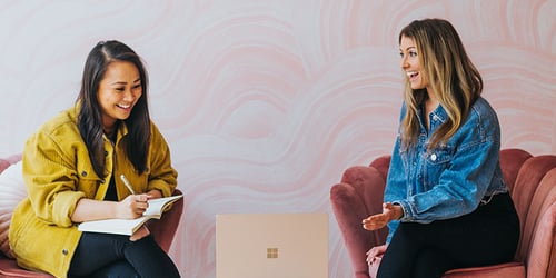 Two people sit beside each other having a conversation about the content on a laptop screen out of view.