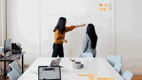 Two people work together in a conference room making notes on a whiteboard. 