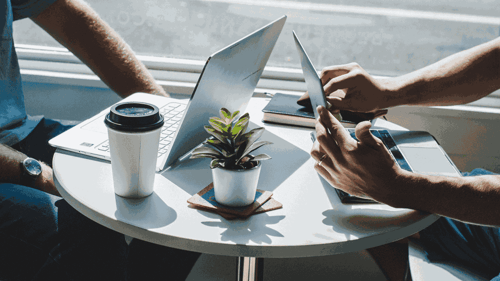 Two people sit across from one another at a table on their laptops and drinking coffee.