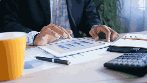 A person sits at their desk reviewing data on a tablet. 