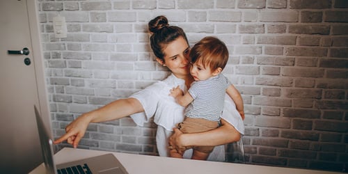 A mother sits on her laptop while also caring for her child.