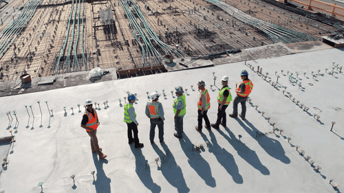 Several people stand on a platform overlooking a construction job site. 