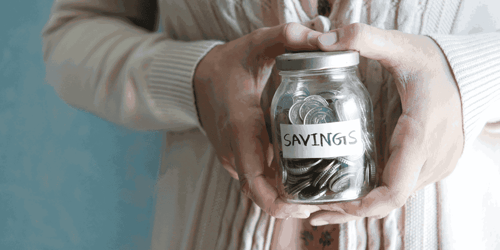 A person with only their hands in view is holding a jar full of coins with the word 