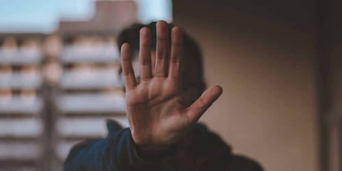 A person stands with their hand up indicating stop.